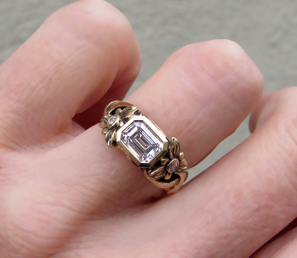 Custom-designed & hand-carved solitaire with 1ct emerald cut diamond. Lily flower, leaves, bulb motif.