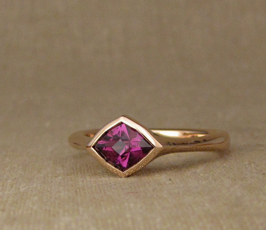 Hand-carved low-profile solitaire for a custom-cut purplish-pink garnet. 14K rose gold.