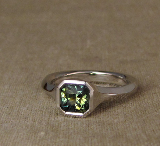 Custom hand-carved geometric solitaire for radiant-cut blue-green parti-sapphire. Platinum.