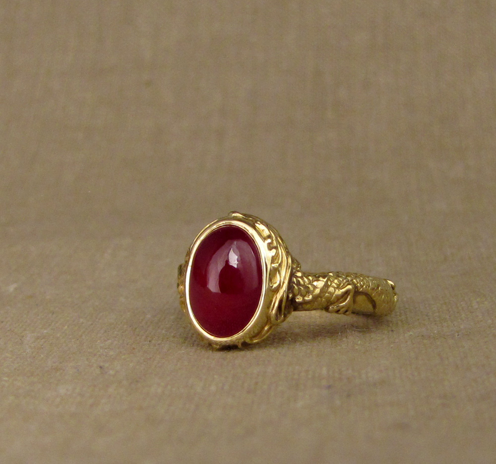 Hand carved ruby cabochon solitaire with Chinese dragon and phoenix chasing each other around the band. 18K yellow gold