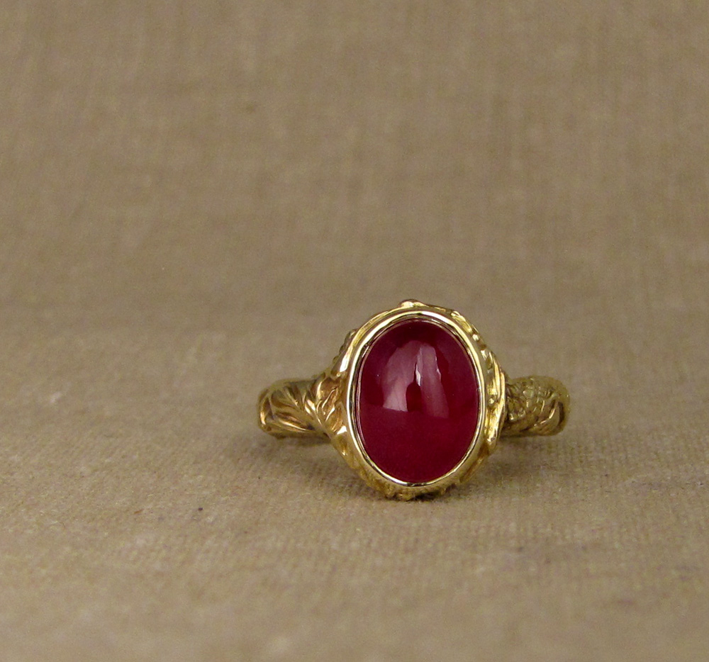 Hand carved ruby cabochon solitaire with Chinese dragon and phoenix chasing each other around the band. 18K yellow gold