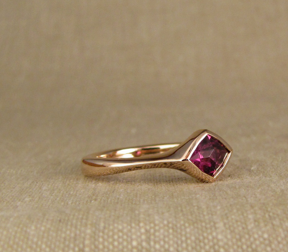Hand-carved low-profile solitaire for a custom-cut purplish-pink garnet. 14K rose gold.