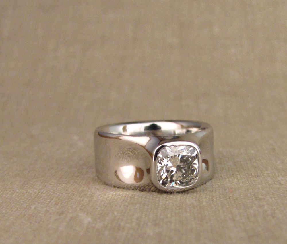 Hand-carved bezel-set cushion diamond in wide platinum band