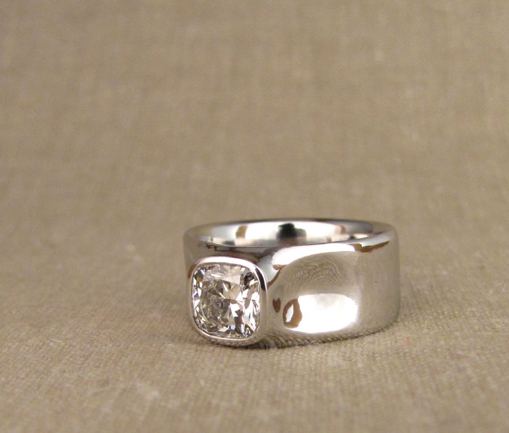Hand-carved bezel-set cushion diamond in wide platinum band